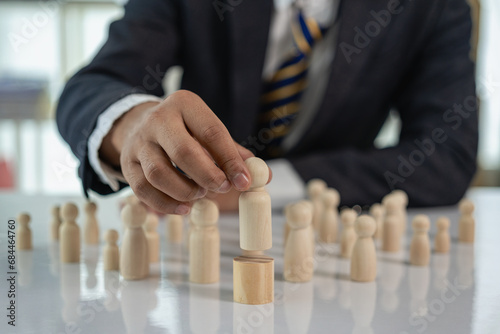 Finger touching a wooden puppet businessman on a wooden cube, personnel selection leadership commander To create strong teamwork for business organizations
