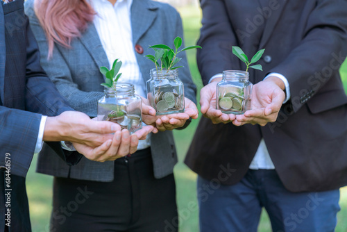Concept of sustainable money growth investment with glass jar filled with money savings coins with businesspeople as eco-friendly financial investment nurtured with nature and healthy retirement. Gyre © Summit Art Creations