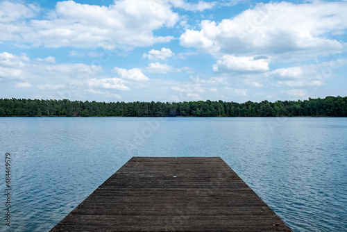 This image presents a tranquil wooden dock leading out to a calm and expansive lake. The simplicity of the composition, with the wooden platform jutting into the water, invites contemplation and a