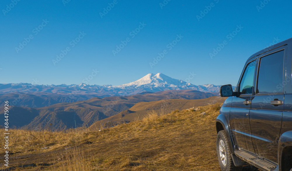 A car against the backdrop of a beautiful landscape, snow-capped Mount Elbrus and blue sky on autumn days