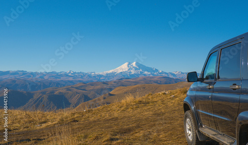 A car against the backdrop of a beautiful landscape, snow-capped Mount Elbrus and blue sky on autumn days © Ekaterina