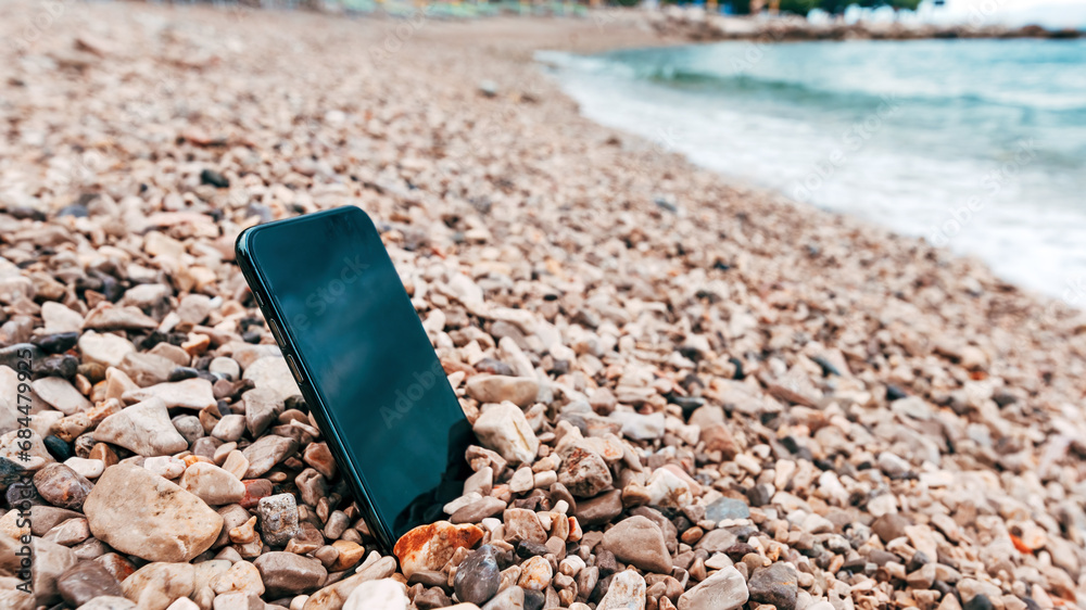Modern new mobile phone lost at the seaside beach in pebbles Modern new mobile phone lost at the seaside beach in pebbles