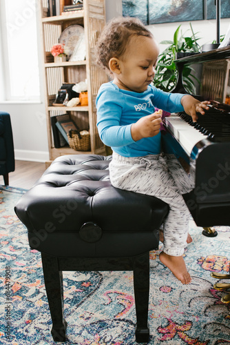 Mixed race toddler boy plays grand piano in home photo