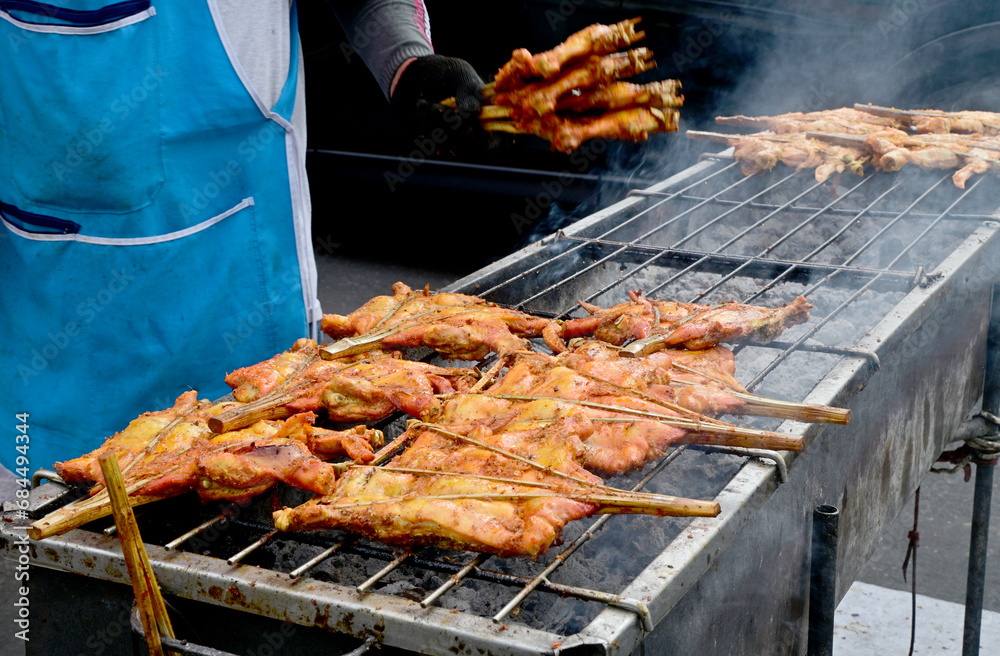 Chicken hips are grilled on a grill on the stove at the street food local market in Thailand.
