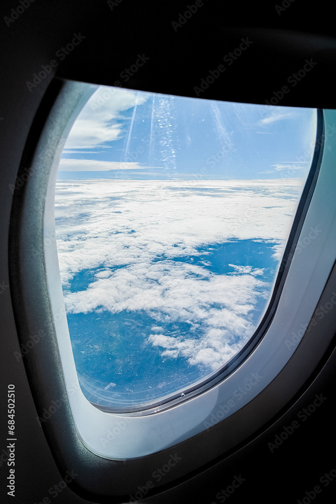 Scenic nature view from an airplane window during flight above white clouds against a blue sky background. Travel concept. Relaxation and enjoying the traveling