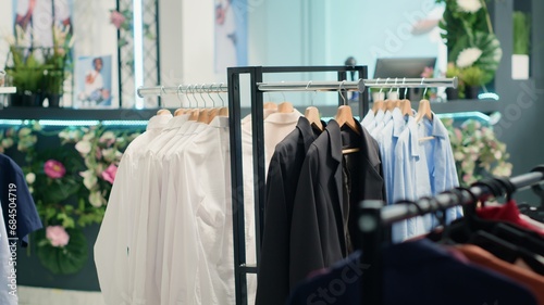 Panning shot of empty luxurious fashion boutique with elegant clothes on racks. Clothing store selling high street men blazers and shirts on hangers for special occasions