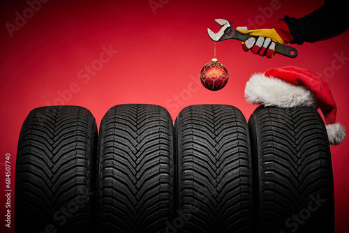 Winter car tires service and hands of mechanic, wrench screwdriver, christmas ball happy new year red background.