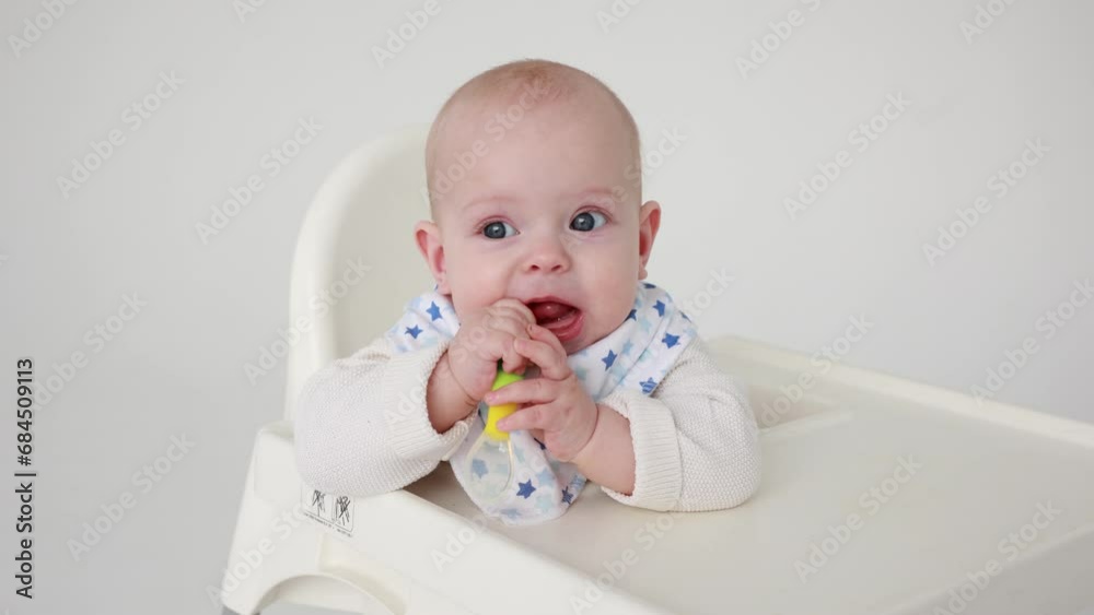 4k, cute baby girl sitting on a feeding chair nibbling a silicone baby spoon looking at the camera, the concept of introducing complementary foods for babies 4k, cute baby girl sitting on a feeding chair nibbling a silicone baby spoon looking at the camera, the concept of introducing complementary foods for babies