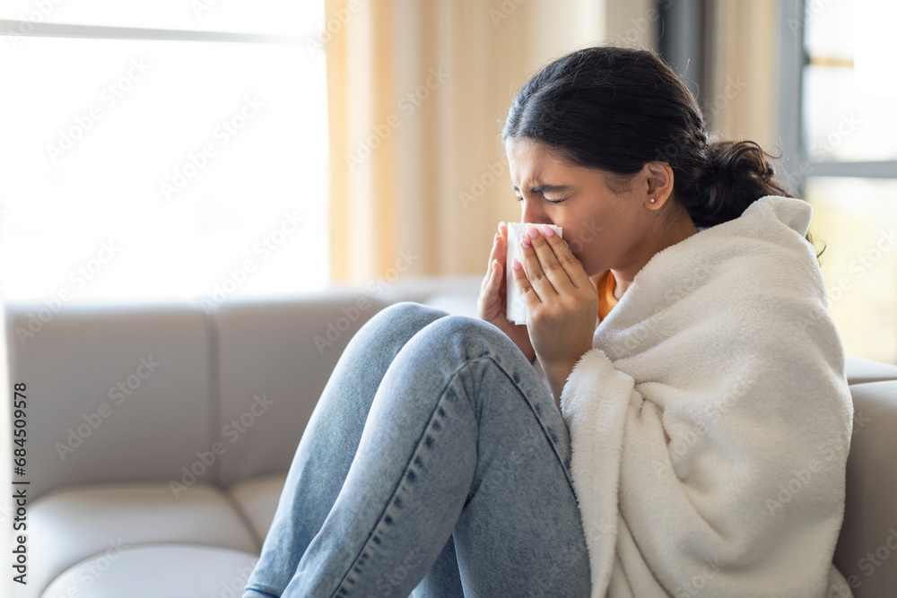 Seasonal Flu. Sick Young Indian Woman Blowing Nose In Tissue At Home