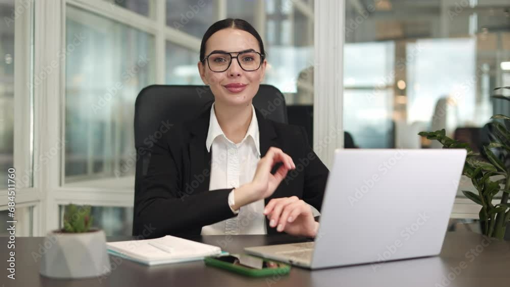 Beautiful successful female sitting in front of wireless devices and adjusting glasses while smiling in office. Cheerful lady dressed in classic style showing harmony and career achievements indoors. Beautiful successful female sitting in front of wireless devices and adjusting glasses while smiling in office. Cheerful lady dressed in classic style showing harmony and career achievements indoors.