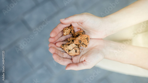 Top view of white hands holding cookies split in several pieces in black paved street floor background