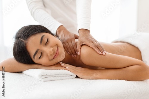 Joyful young indian woman receiving relaxing shoulder massage