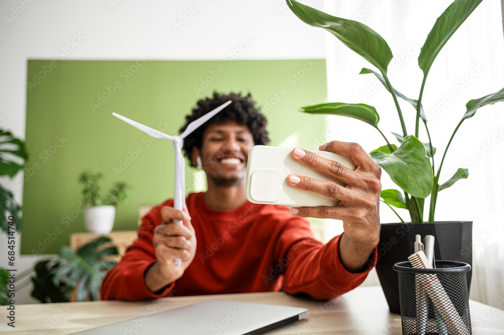 Freelancer taking selfie with wind turbine through smart phone at home office