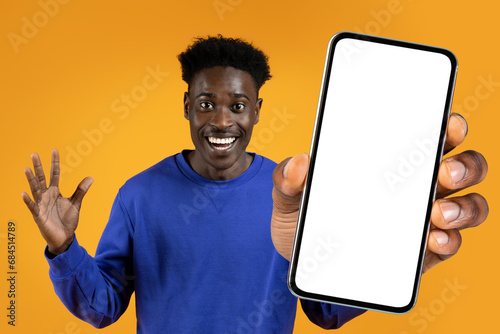 black guy offering huge smartphone with blank screen, orange backdrop