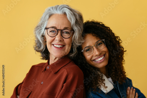 Smiling mother and daughter wearing eyeglasses against yellow background photo
