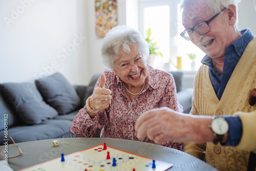 Cheerful woman gesturing thumbs up and playing ludo with man at table photo