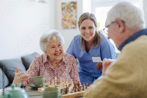 Happy healthcare worker with senior couple playing chess photo