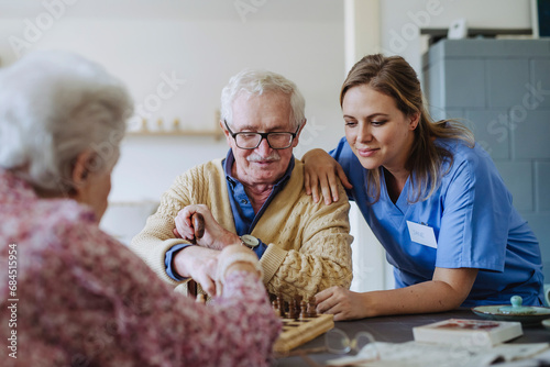 Smiling healthcare worker playing chess with senior couple at home photo