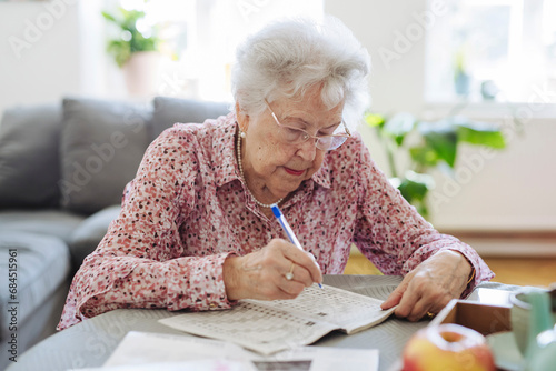 Senior woman with pen doing crossword puzzle in book at table photo