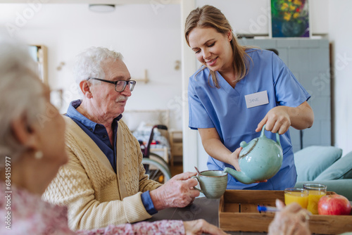 Smiling healthcare worker serving tea to senior couple sitting at table