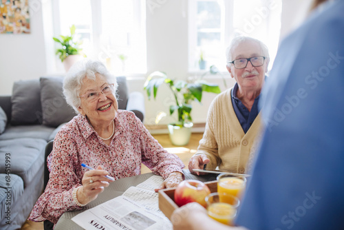 Happy senior couple with healthcare worker holding tray of apple and glasses of juice at home photo
