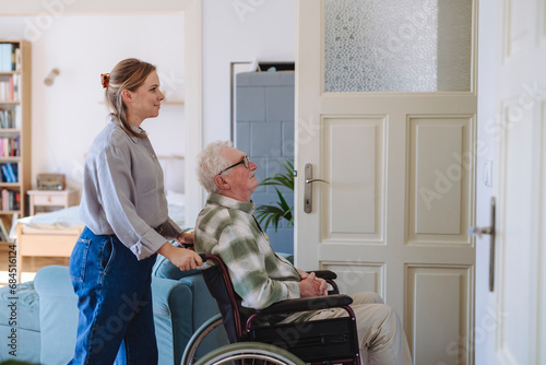 Smiling healthcare worker with man sitting in wheelchair at home photo