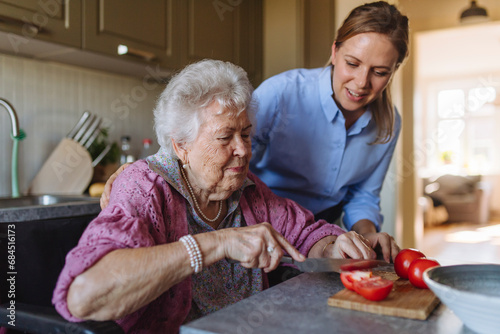 Senior woman cutting tomatoes with smiling home caregiver