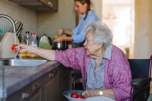 Senior woman washing tomatoes with home caregiver working in background photo