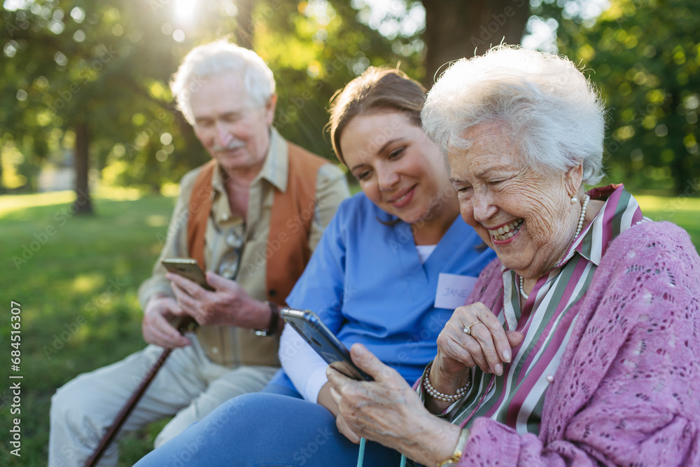 Happy healthcare worker with senior man and woman using smart phone in park Happy healthcare worker with senior man and woman using smart phone in park