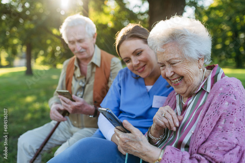 Happy healthcare worker with senior man and woman using smart phone in park photo
