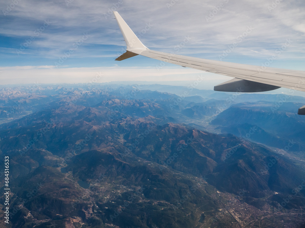 View from an airplane window of a mountain area and left wing, warm sunny day. Travel and tourism view. Flying to holiday destination point. Scene through illuminator. High viewpoint. View from an airplane window of a mountain area and left wing, warm sunny day. Travel and tourism view. Flying to holiday destination point. Scene through illuminator. High viewpoint.
