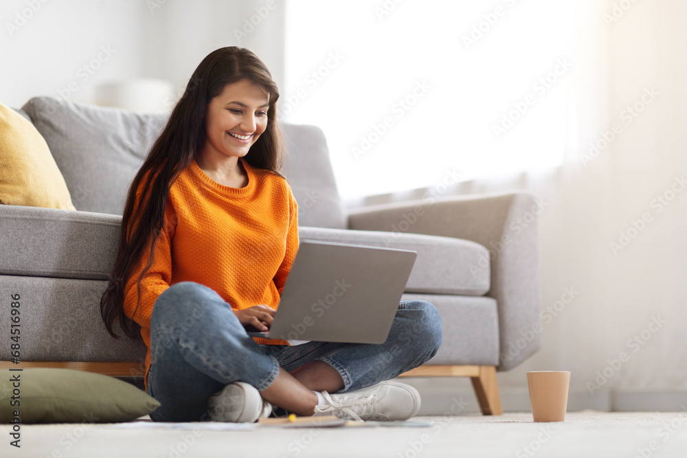 Cheerful young indian woman using laptop, home interior Cheerful young indian woman using laptop, home interior