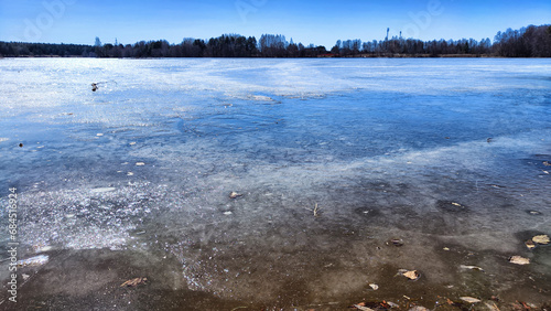 Landscape with a lake covered with ice before the start of melting and ice drift on a spring day with the sun. Blue ice and water under sunlight in early spring or autumn