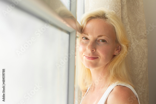 Smiling blond woman leaning on window at home photo