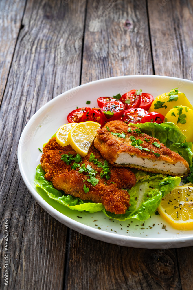 Crispy breaded fried chicken cutlet with fresh vegetables and boiled potatoes on wooden table
