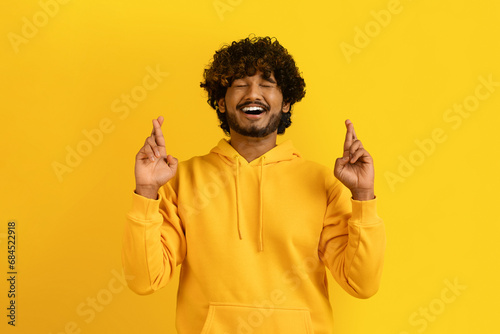 Superstitious indian guy with closed eyes and crossed fingers photo