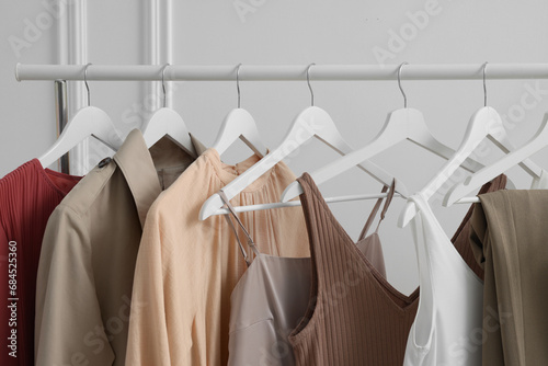 Rack with different stylish women`s clothes near white wall indoors, closeup
