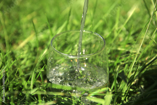 Pouring pure water into glass in grass outdoors on sunny day