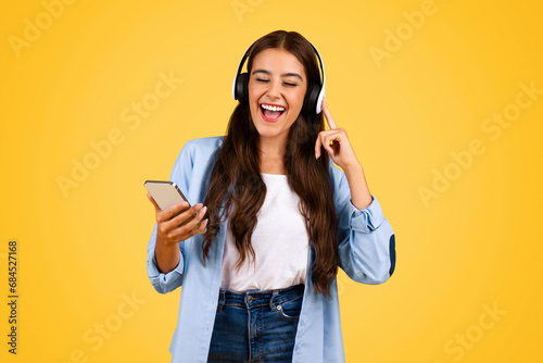 Happy teenager student woman typing on smartphone with headphones, sing song photo