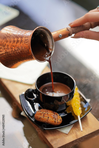 Coffee pouring from a Turkish copper coffee pot into a black coffee cup.