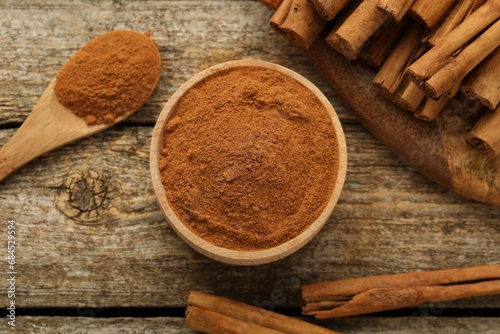 Bowl of cinnamon powder and sticks on wooden table, flat lay photo
