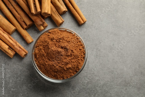 Bowl of cinnamon powder and sticks on grey table, flat lay. Space for text