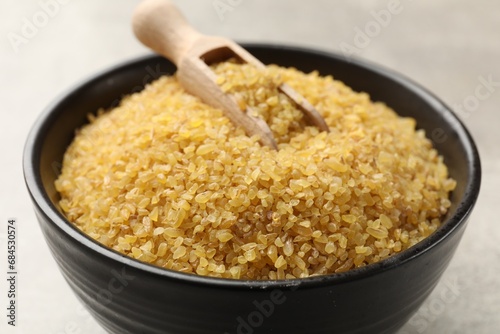 Bowl and scoop with raw bulgur on gray background, closeup