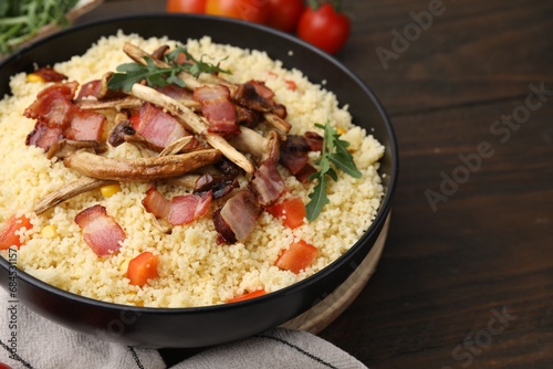 Tasty couscous with mushrooms and bacon in bowl on wooden table, closeup. Space for text