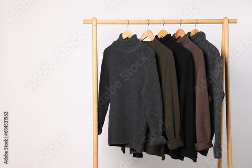 Rack with different casual sweaters on light background. Space for text