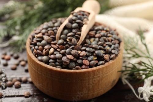 Raw lentils and scoop in bowl on wooden table, closeup photo