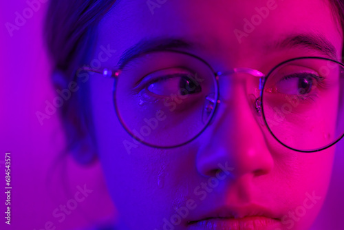 Cute girl with glasses crying in neon light, face close-up.