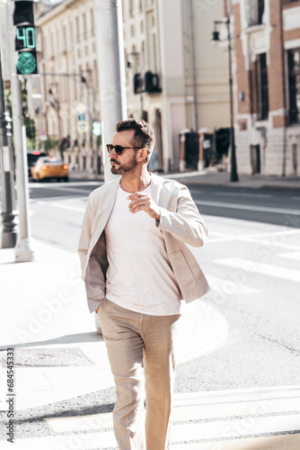 Handsome confident stylish hipster lambersexual model. Sexy modern man dressed in elegant white suit jacket. Fashion male posing in the street background in Europe city at sunset. In sunglasses photo