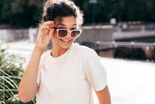 Young beautiful smiling hipster woman in trendy summer white t-shirt and jeans clothes. Carefree woman, posing in the street at sunny day. Positive model outdoors. Cheerful and happy. In sunglasses © halayalex
