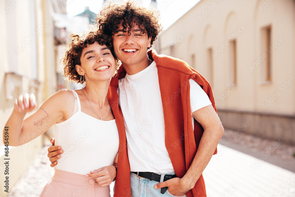Naklejka premium Young smiling beautiful woman and her handsome boyfriend in casual summer white t-shirt and jeans clothes. Happy cheerful family. Female having fun. Couple posing in the street background. Walking